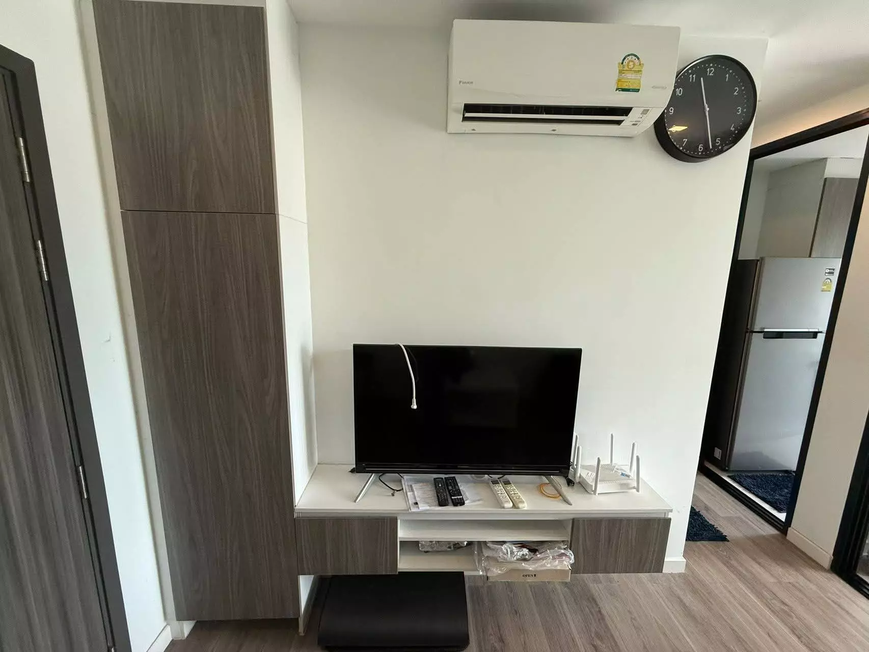 Living area in B Loft Sukhumvit 107 featuring a built-in wardrobe, floating TV console, and an open view into the kitchen