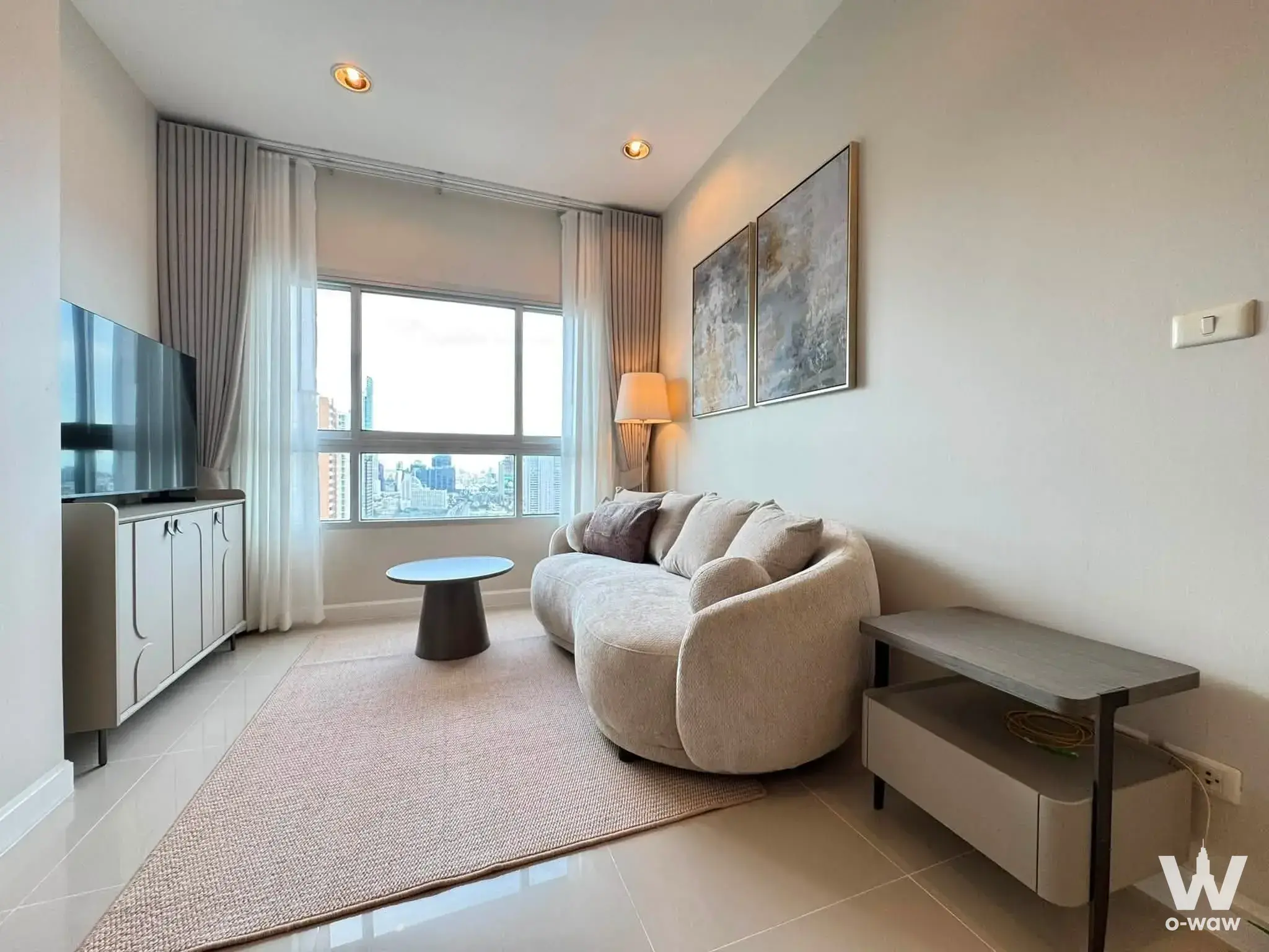 Living room in Q House Condo Sathon with curved beige sofa and city skyline view