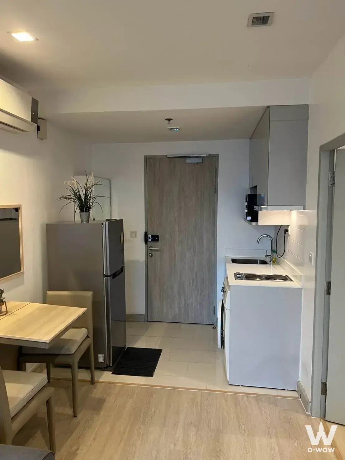 Ideo Mobi Rama 9 studio dining area with light wood table, kitchenette, and smart lock entry