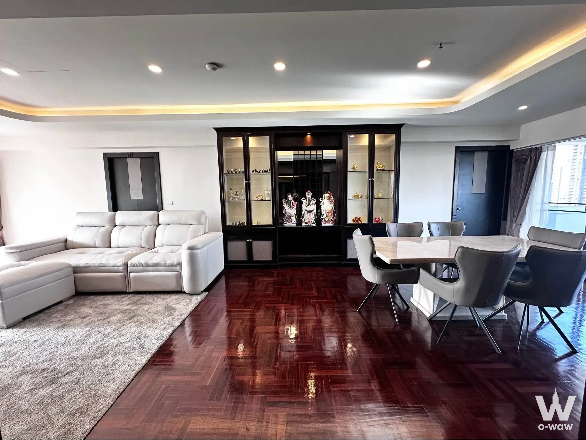 Spacious living room in a Riverside Villa condo with herringbone parquet floors and an L-shaped cream leather sectional sofa