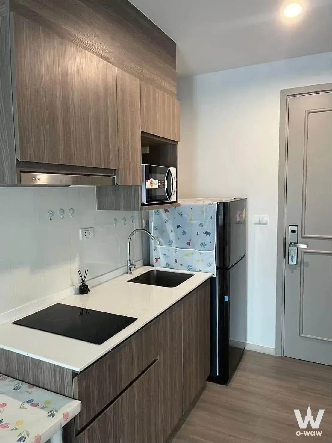 Compact kitchenette in The Parkland Bangna 1-bed condo for rent has wood cabinets and an induction cooktop