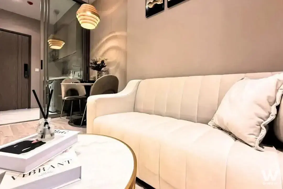 Living room in a Rhythm Ekkamai rental featuring a cream velvet sofa, marble coffee table and warm wooden pendant light