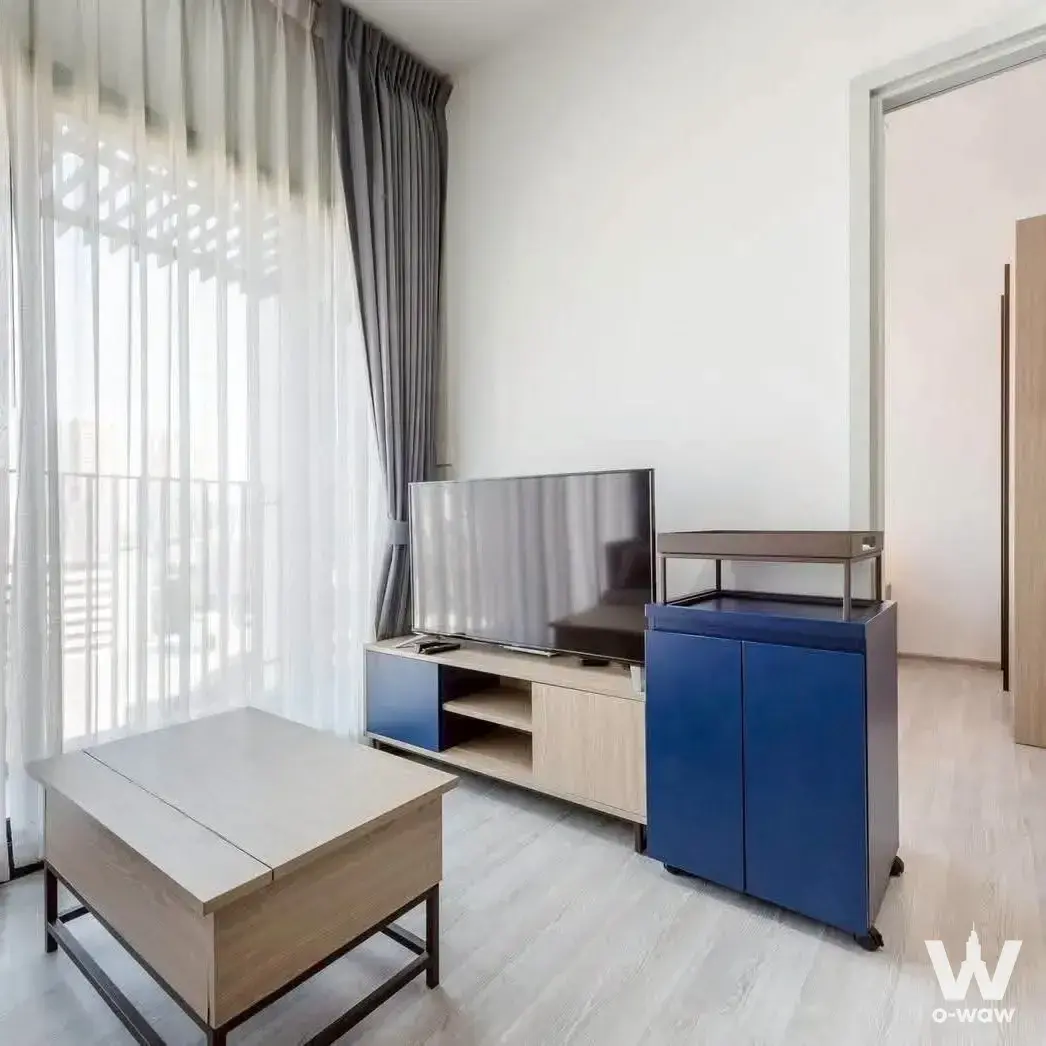 Minimalist living space in an XT Ekkamai 1-bed condo showcasing light wood floors and blue accents