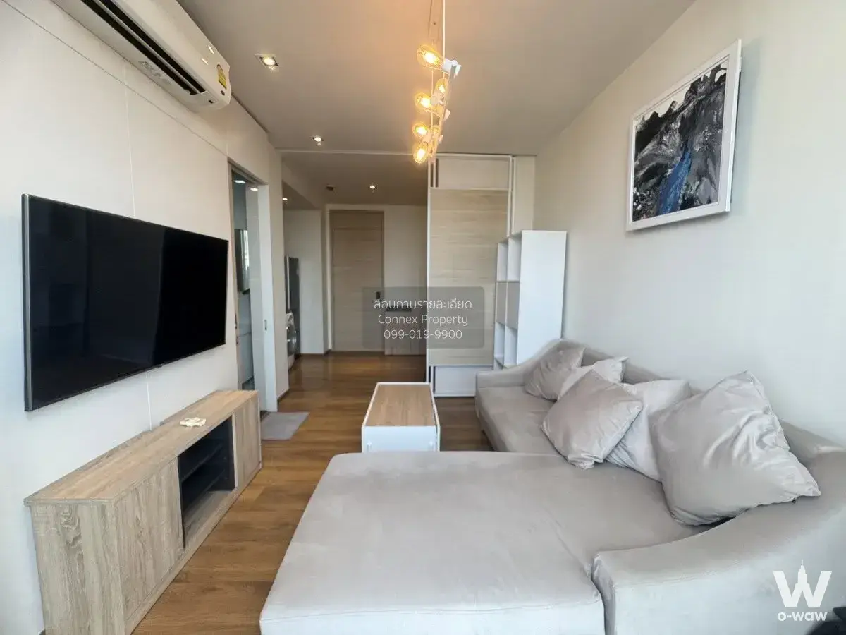 Furnished living room in a Park Origin Phrom Phong rental with a beige L-shaped sofa and wall-mounted flat-screen TV