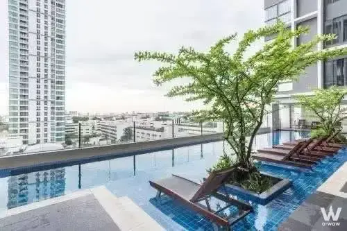 Rooftop infinity pool at Ideo Mobi Phaya Thai featuring blue mosaic tiles and wooden lounge chairs