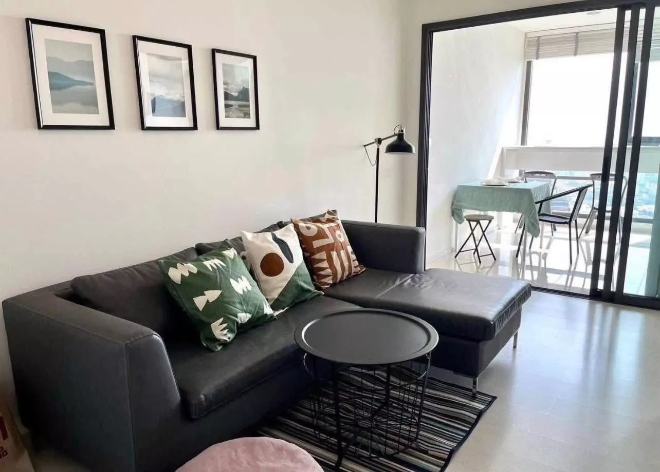 Dark grey sectional sofa facing a balcony with city views in this 1-bed condo for rent at Rhythm Sukhumvit 42