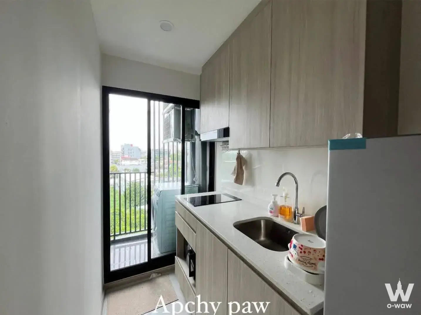 Modern kitchen with light wood cabinets and black cooktop in a 1-bed condo for rent at Origin Play Sri Udom Station