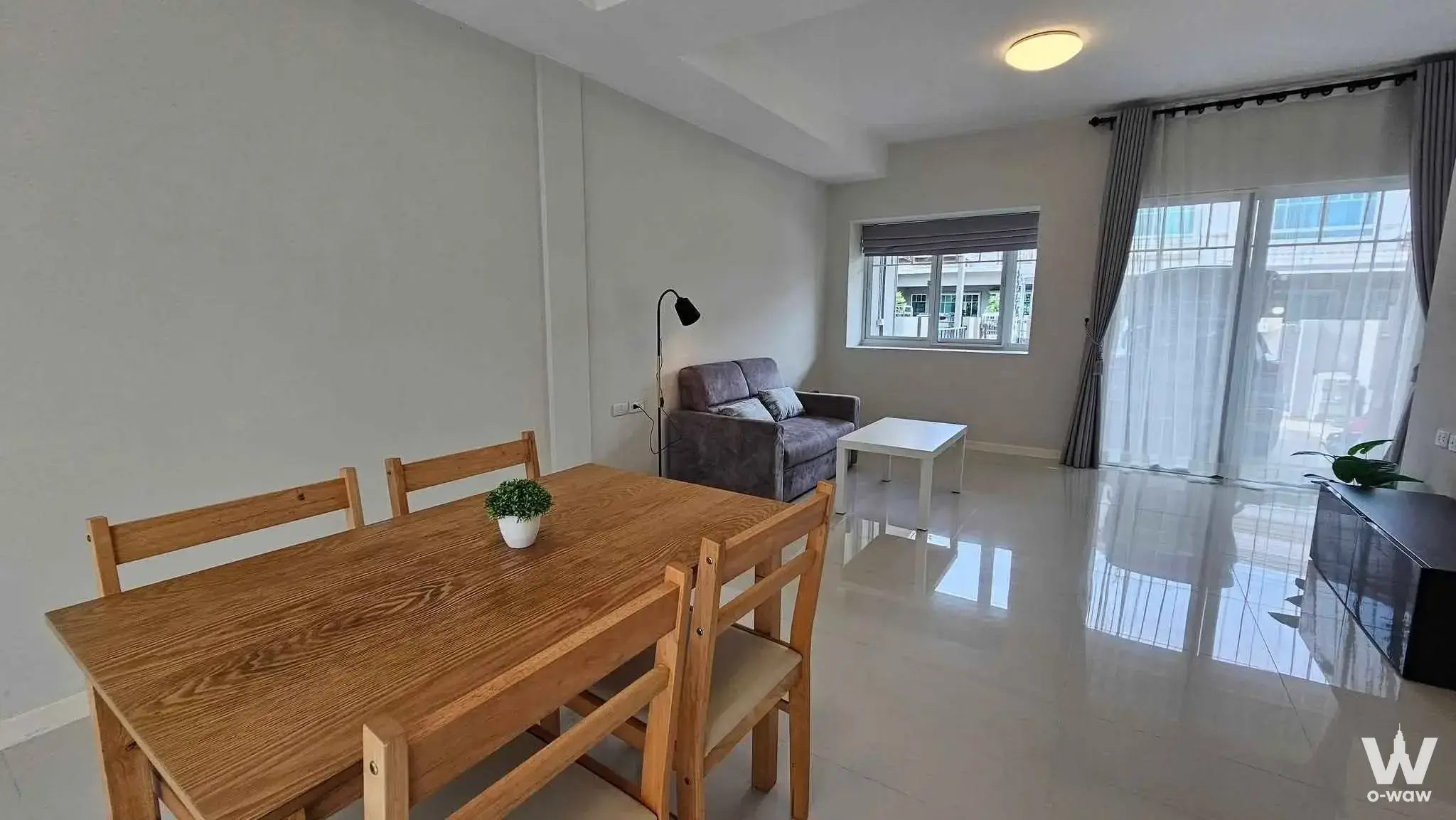 Furnished dining area in a Srinakarin house with oak table and grey sofa near sliding glass doors