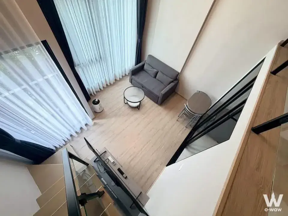 This loft studio in a 1-bed Origin Plug & Play Nonthaburi Station condo for rent has a grey sofa and floor-to-ceiling windows