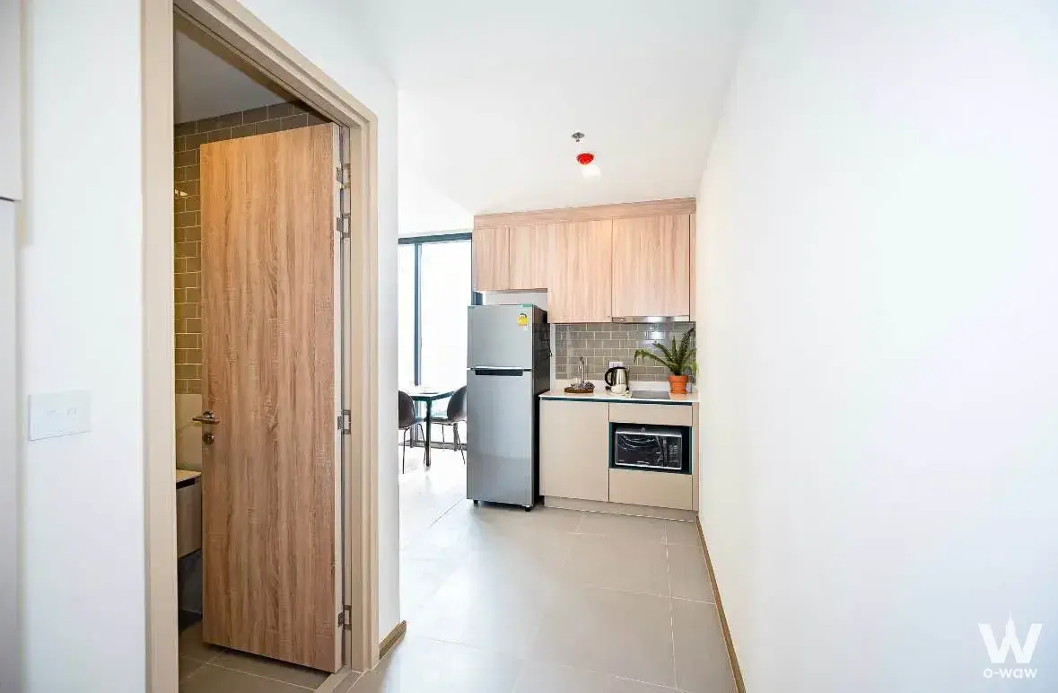 Modern kitchenette with light wood cabinets and black countertop in a 1-bed condo at XT Phayathai