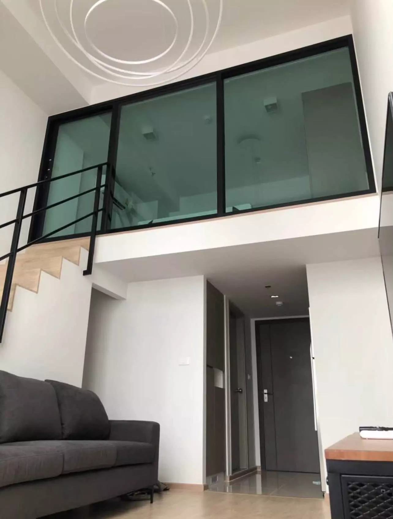 Double-height living room with dark sofa and open staircase in Ideo New Rama 9 1-bed duplex condo