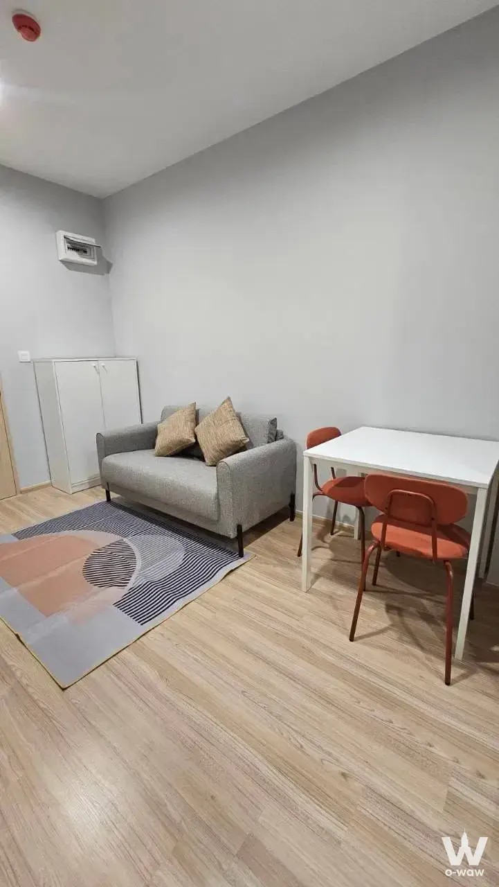 Skyrise Avenue Sukhumvit 64 1-bed condo living area with geometric rug, orange chairs, and minimalist decor