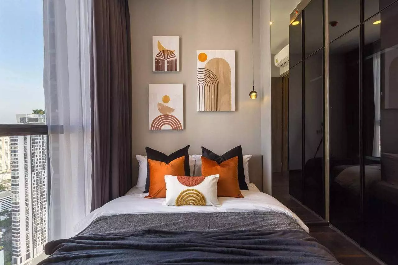 Queen bed with burnt orange velvet pillows and mirrored wardrobe in this Thonglor condo