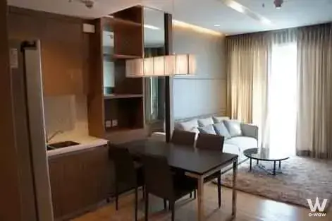 Open-plan living space in Siri at Sukhumvit featuring grey sofa and dark wood dining table