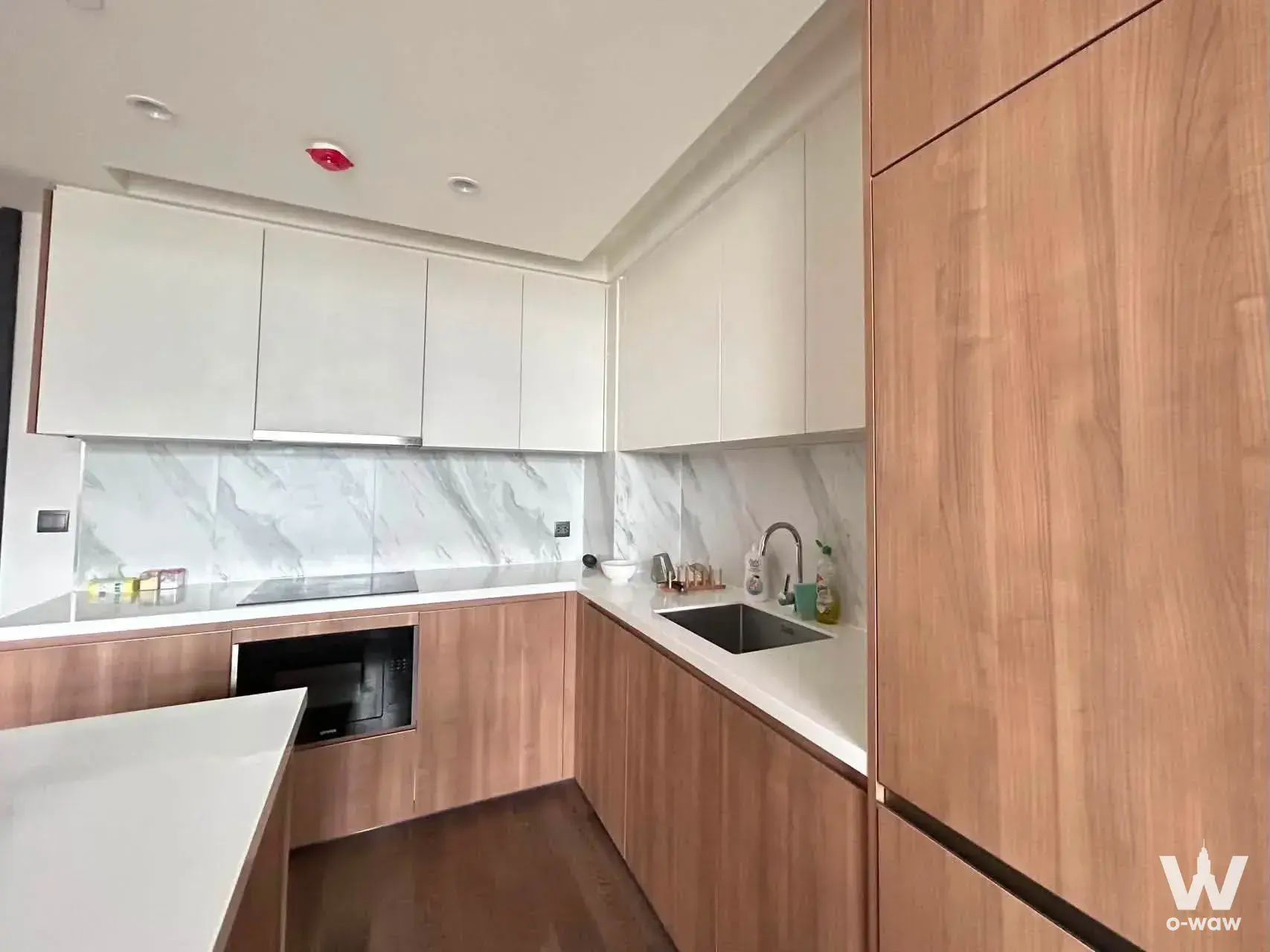 L-shaped kitchen with light wood cabinets and white quartz counters in a 2-bed MUNIQ Sukhumvit 23 condo