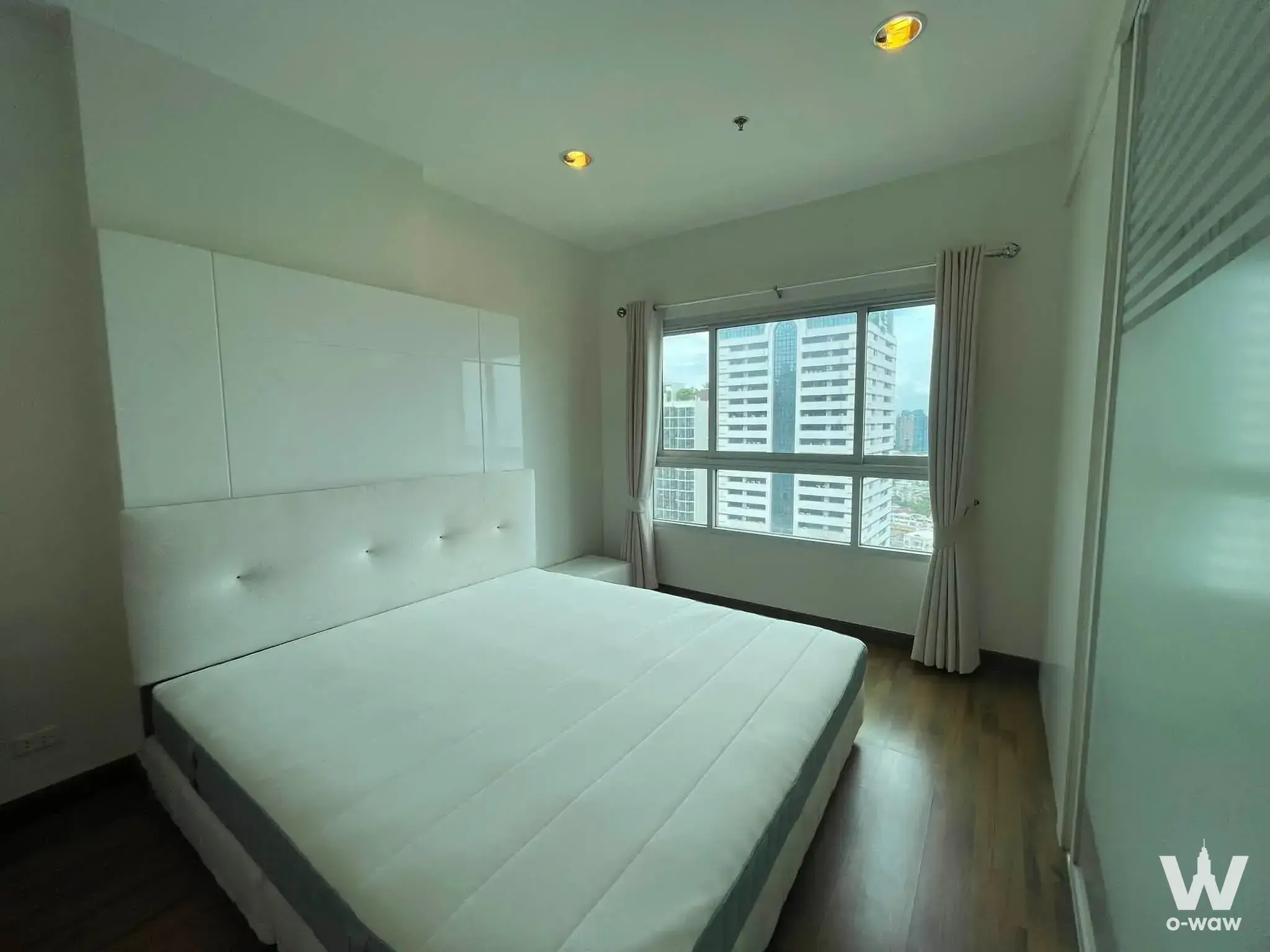 Minimalist bedroom in Q House Condo Sathon with a tufted headboard, dark wood floors, and a frosted glass wardrobe