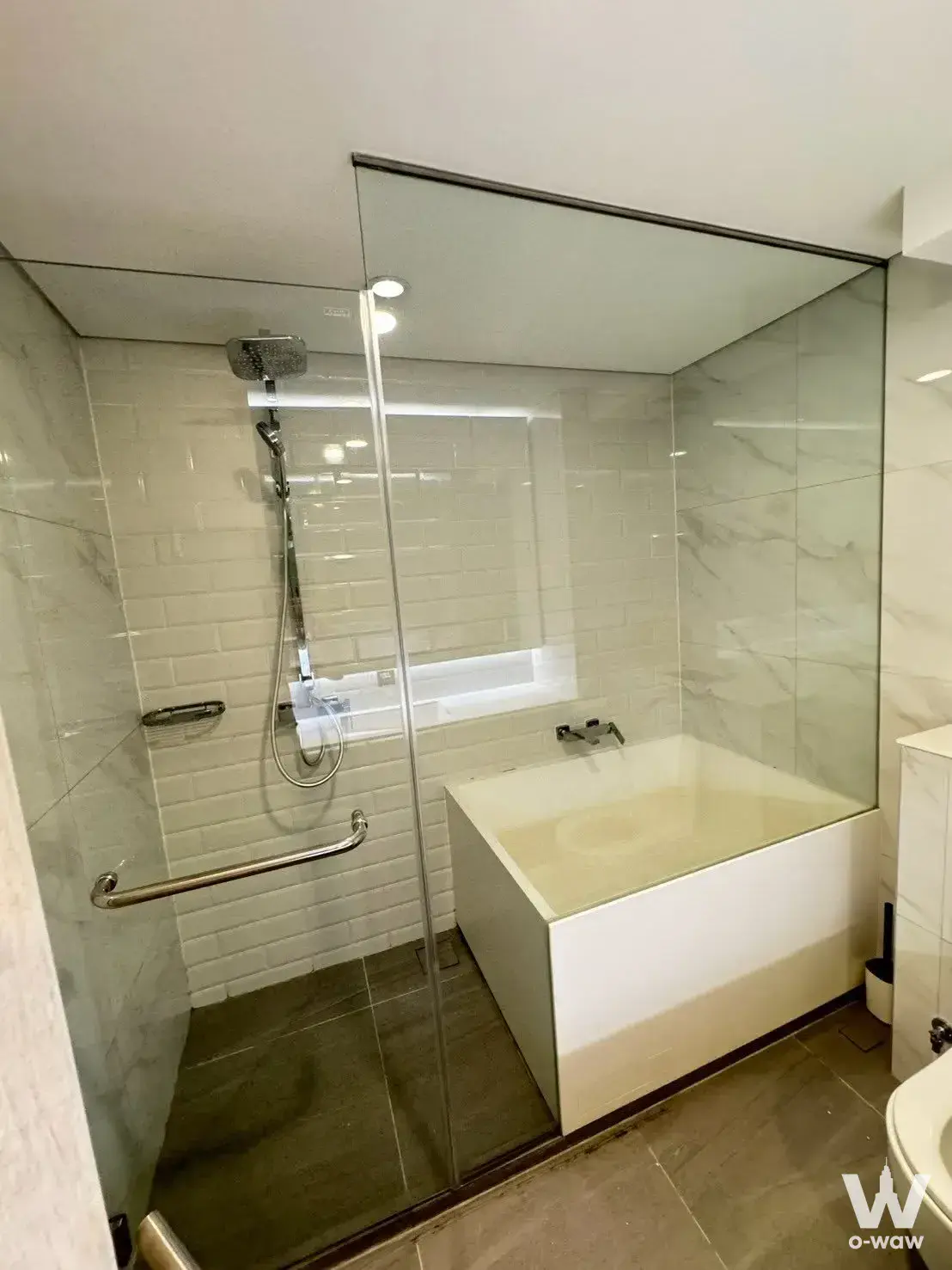 This bathroom in a Siamese Residence one-bed condo has a glass walk-in shower, rain head and white bathtub