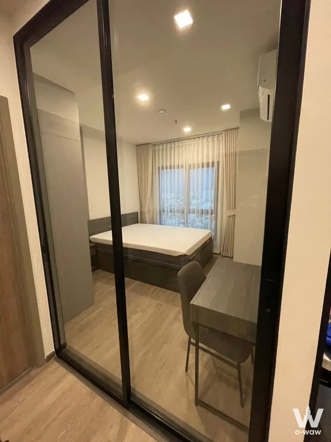 Minimalist bedroom in M Ladprao condo featuring queen bed and city view through sheer curtains