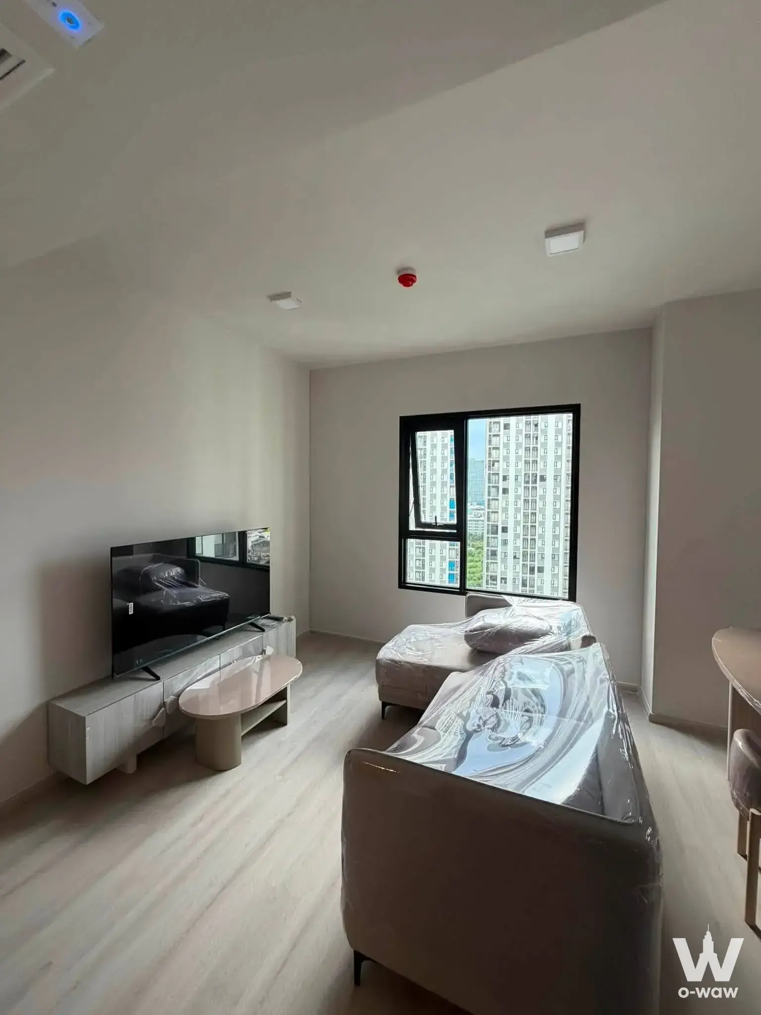 Newly furnished living room in COBE Ratchada-Rama 9 with beige sofa set and large city-view window