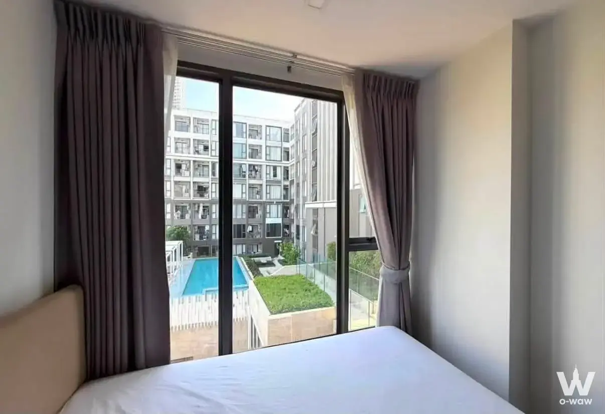 Queen bed with floor-to-ceiling window overlooking the pool in this 1-bed rental at The Nest Sukhumvit 64