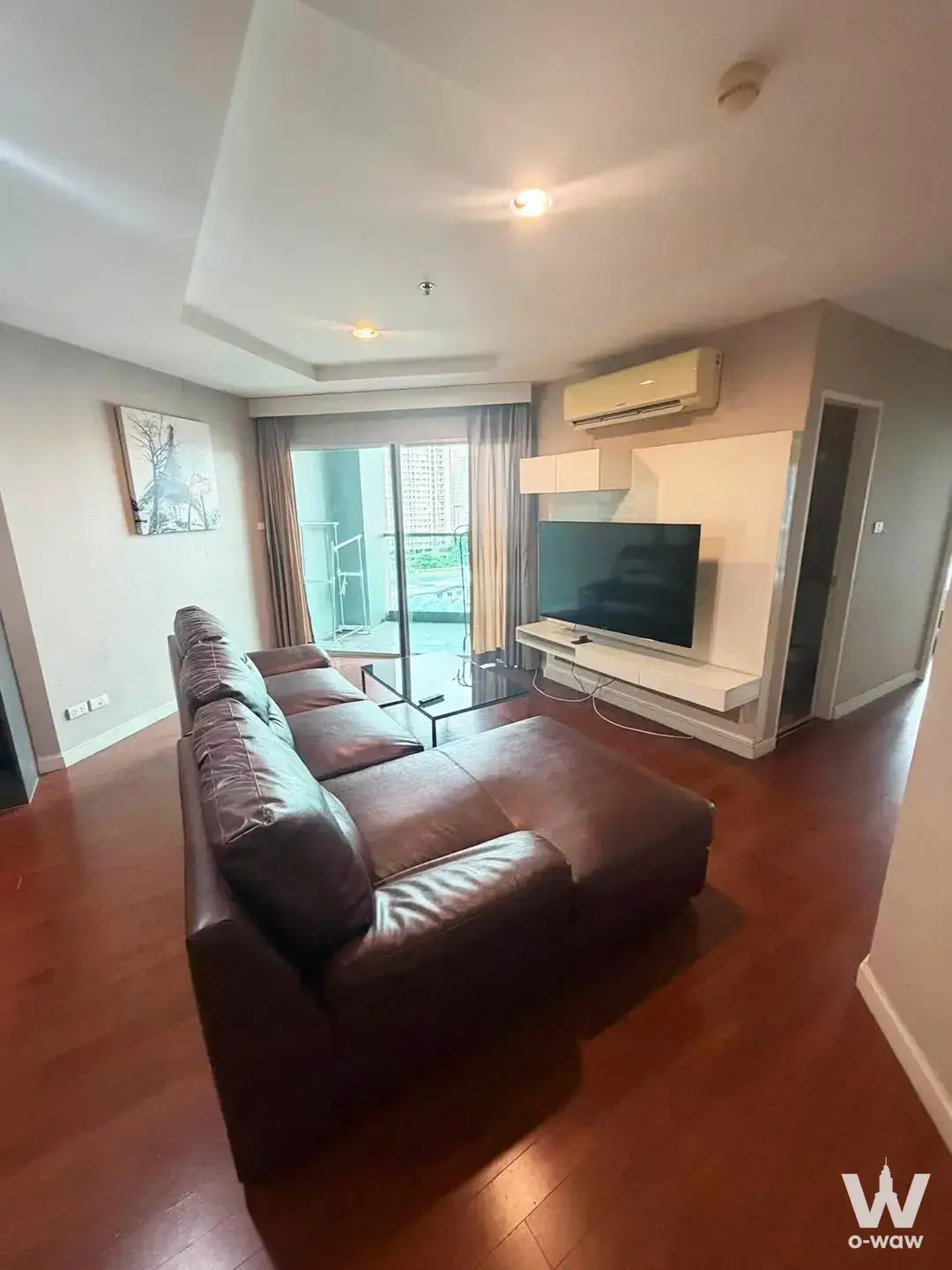 Modern living room in Belle Grand Rama 9 with brown leather sectional and glass door leading to balcony