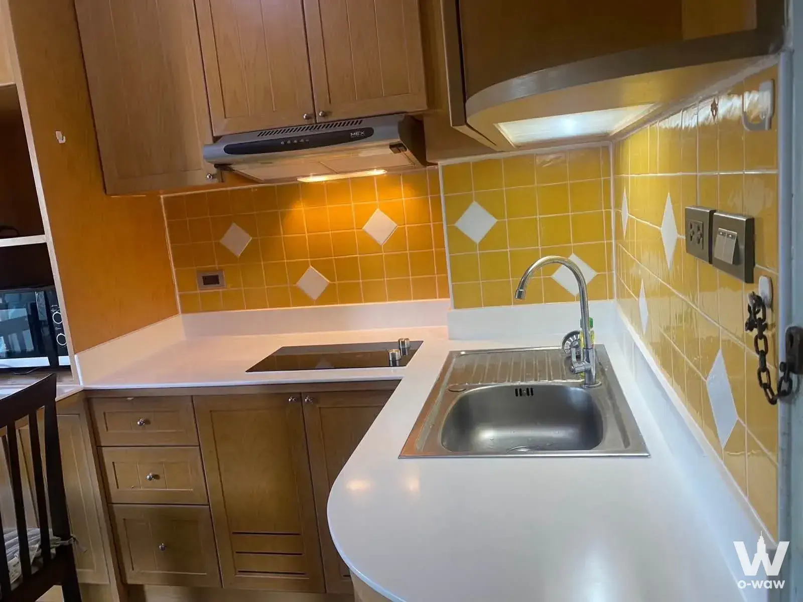 Compact L-shaped kitchen in The Parkland Bangna condo with light oak cabinets and a yellow tile backsplash