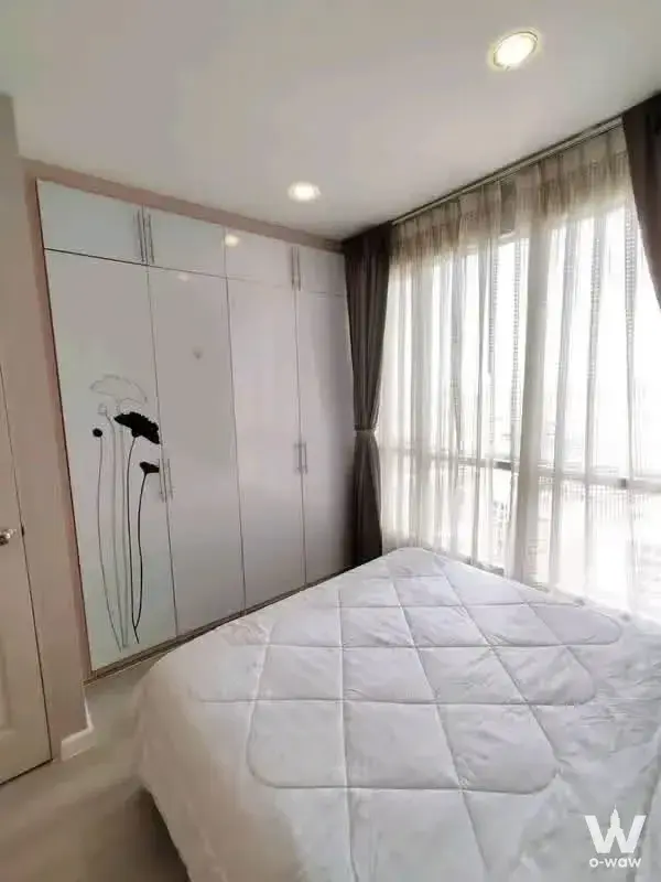 Bright bedroom in a 1-bed Life@Ratchada condo featuring a large white wardrobe and queen bed