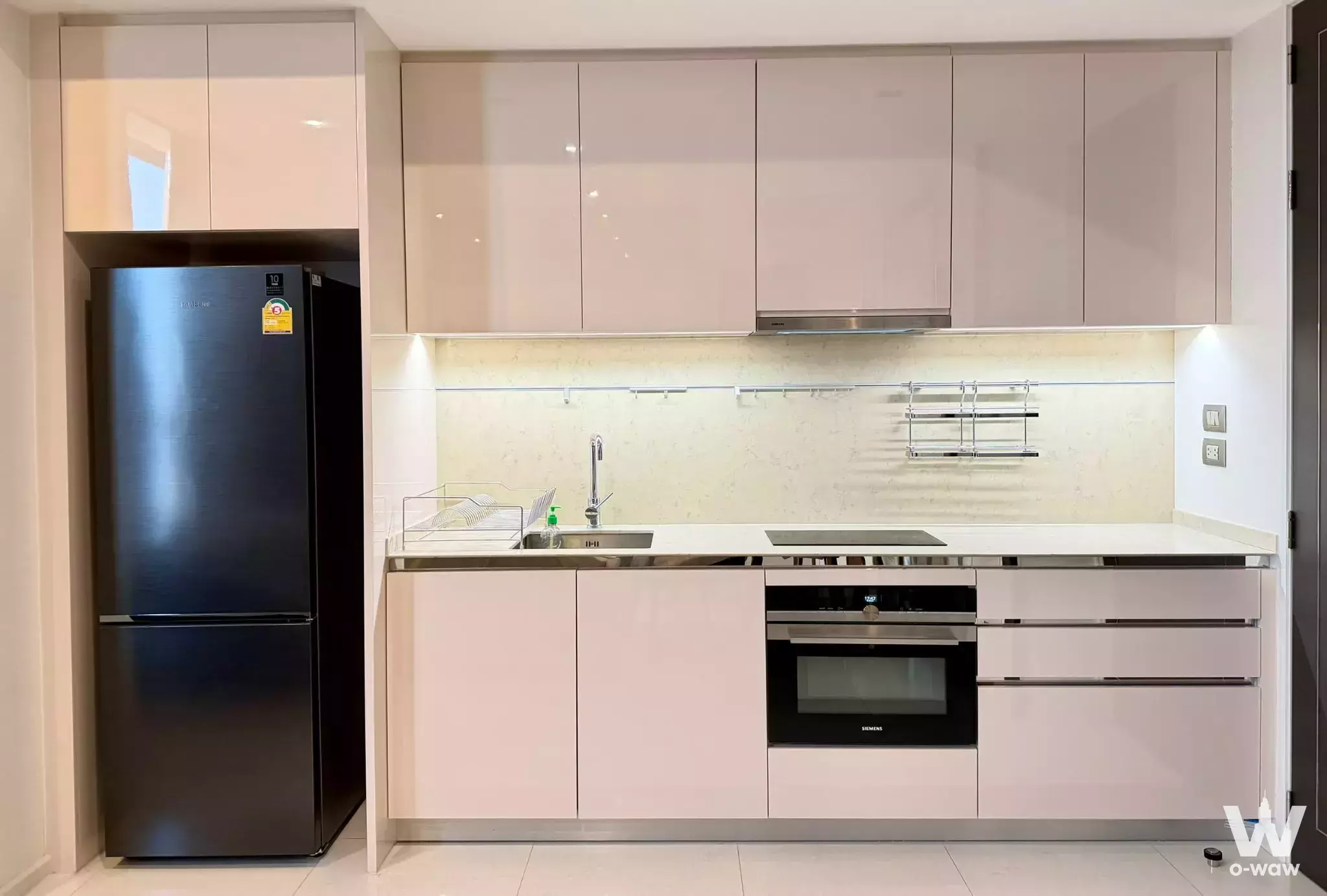 Modern kitchen in The Bangkok Sathorn condo featuring taupe handleless cabinets and black appliances