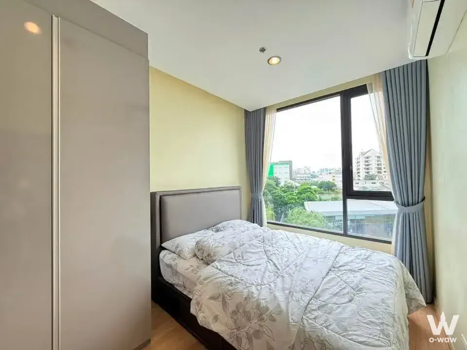 Skyrise Avenue Sukhumvit 64 1-bed condo bedroom with oak flooring, yellow accent wall, and city views