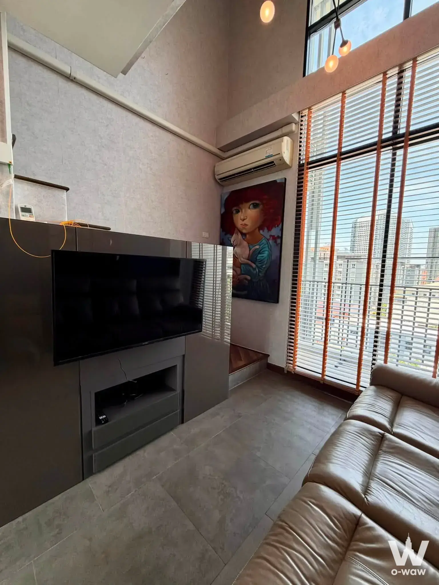 Industrial-chic living room in Beyond Sukhumvit condo with exposed concrete, tan leather sofa, and red artwork