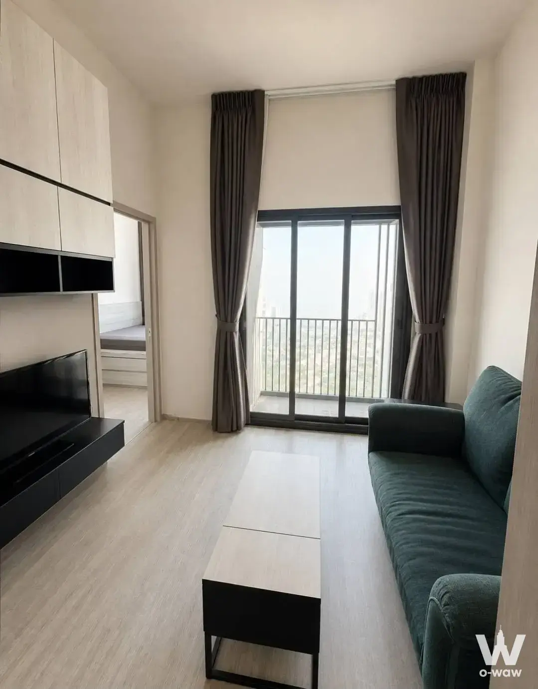Living room with teal sofa and balcony city view in a 1-bed condo for rent at THE LINE Sukhumvit 71