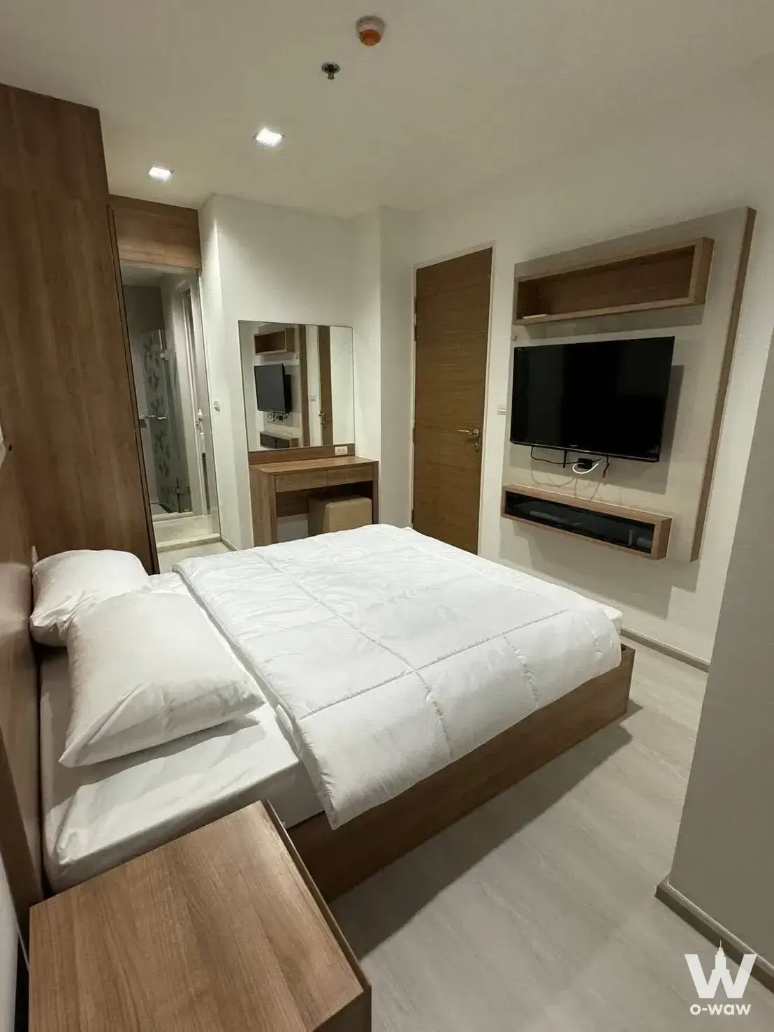 RHYTHM Phahon-Ari bedroom with low-profile queen bed, floating wood shelves, and an open view to the bathroom