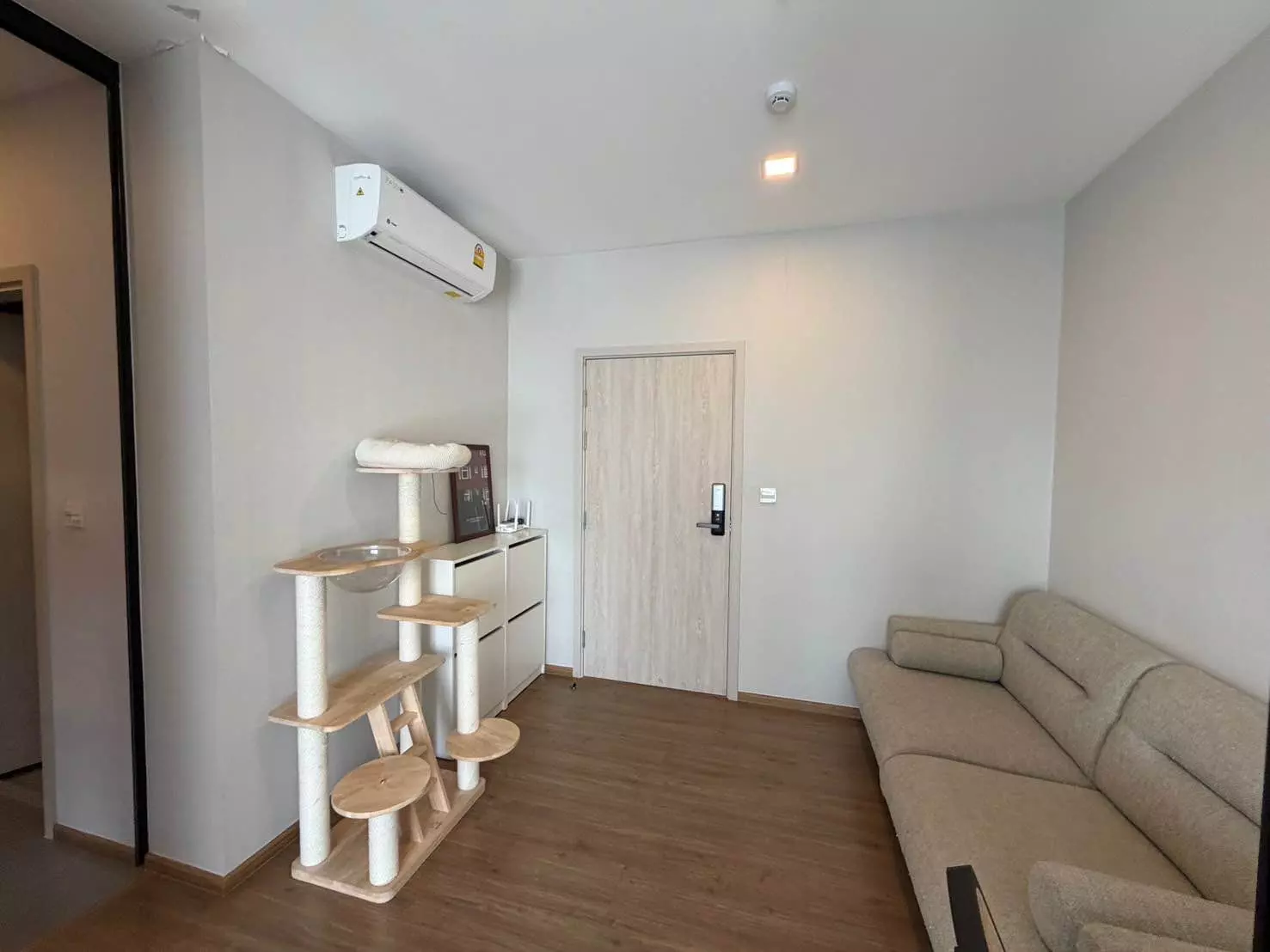Living room in a Metris Rama 9 condo with beige sofa, wooden cat tree, and smart lock entry door