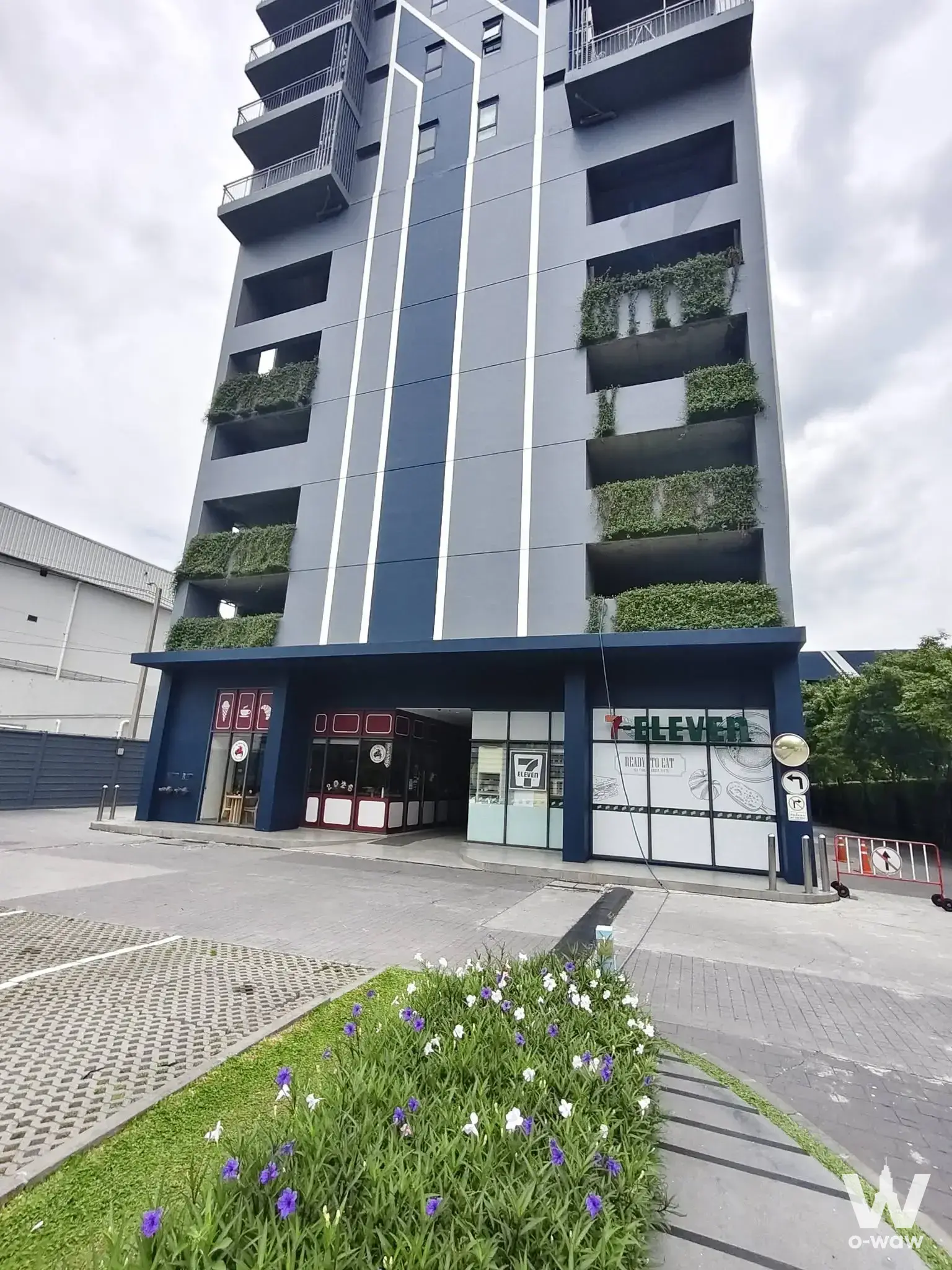 Exterior of IDEO Sukhumvit 115 showing dark facade, balconies, and ground floor 7-Eleven storefront
