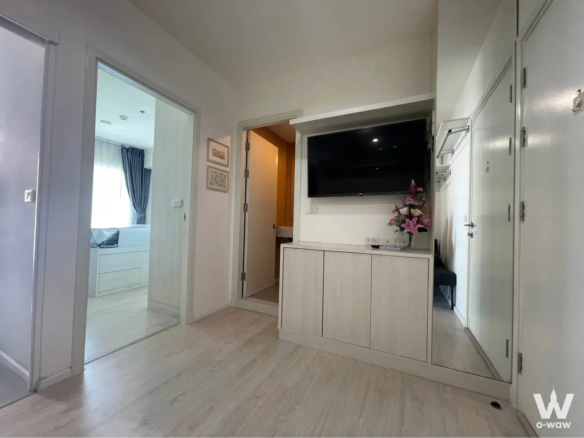 Entry hallway in Aspire Sathorn - Tha Phra condo with built-in TV unit, light wood laminate, and white storage closets