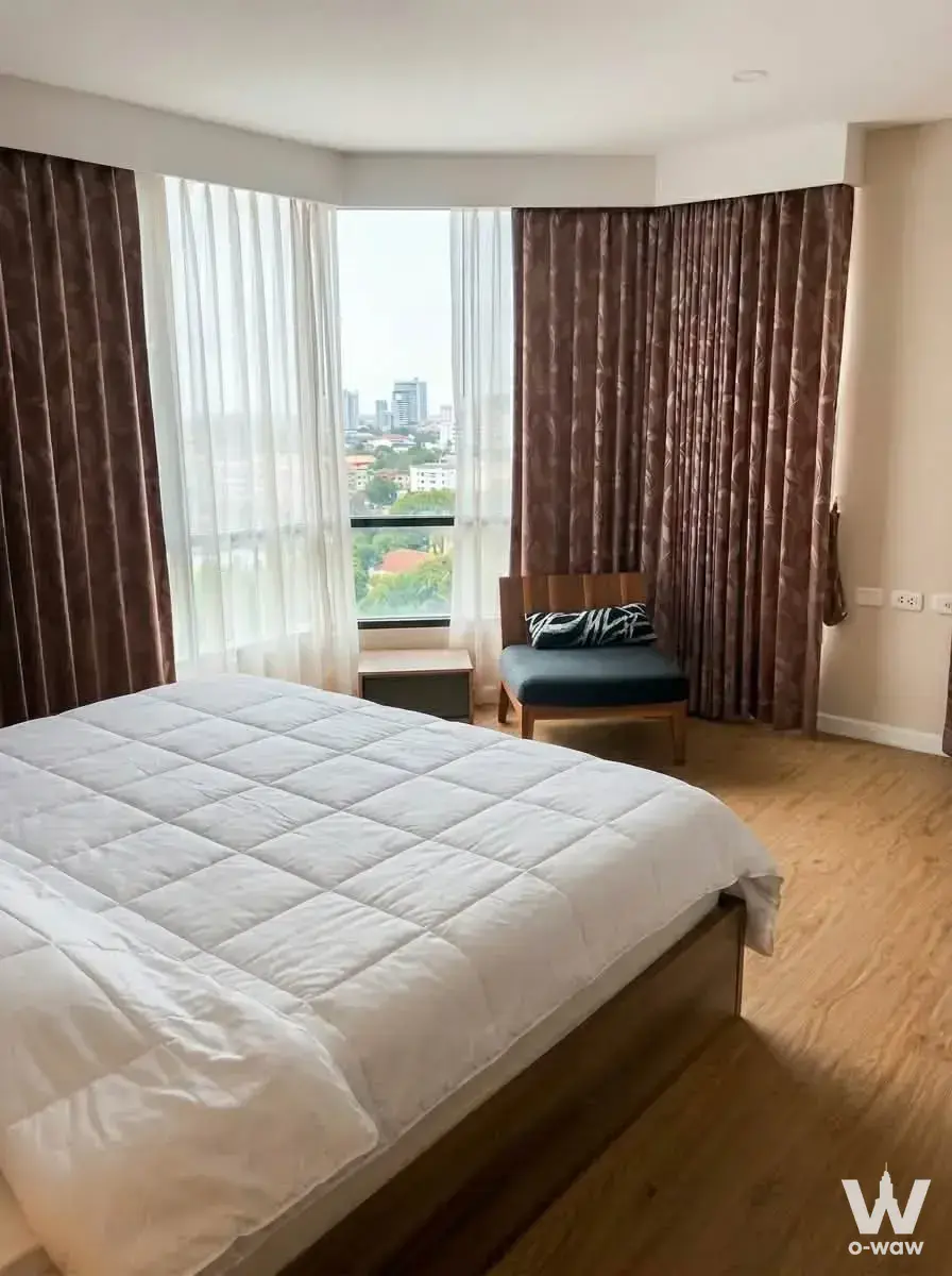 Bedroom with wooden platform bed and bay window view in Siamese Nang Linchee condo