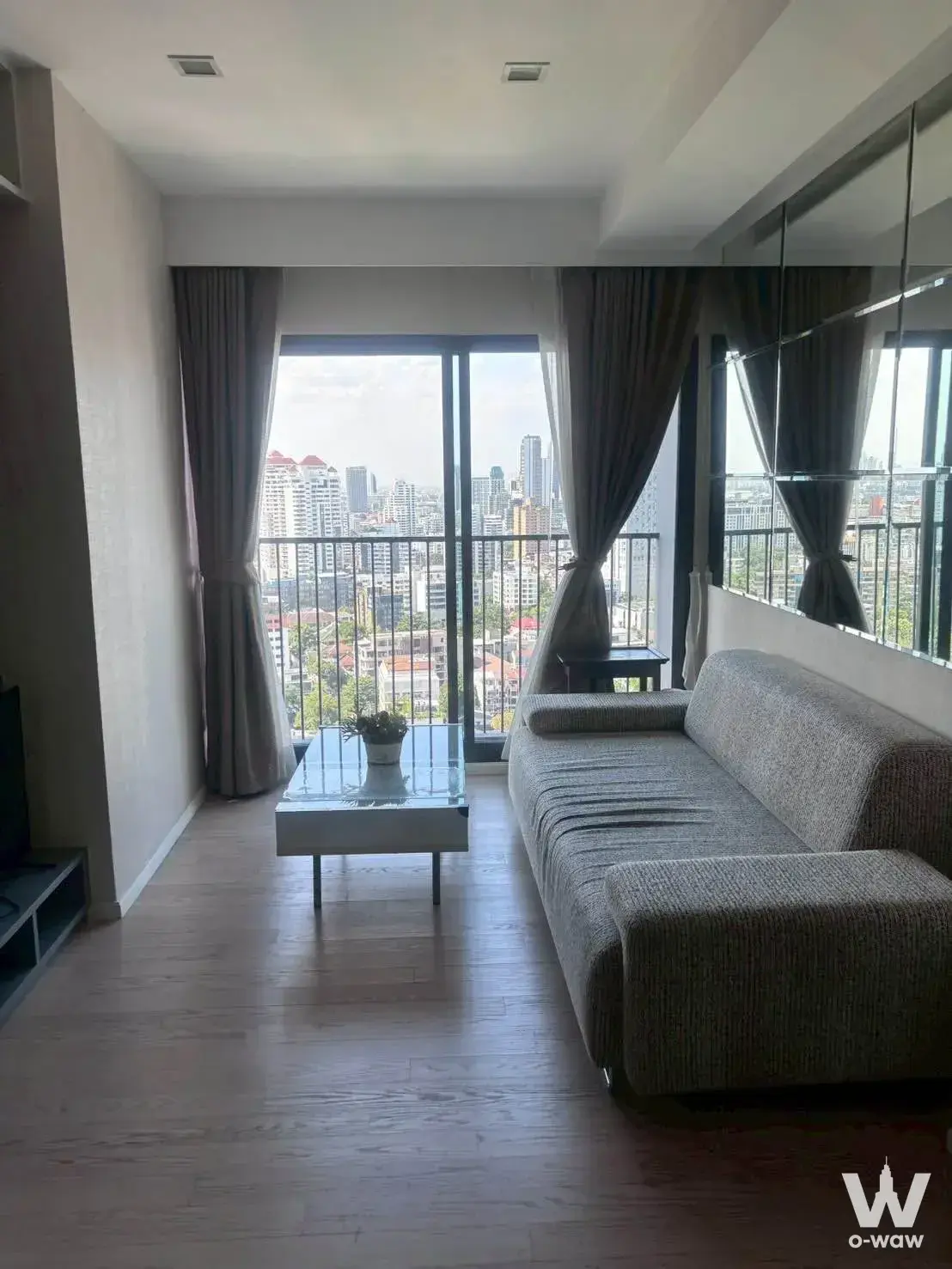 Grey sofa and mirrored wall panel in a furnished 1-bed condo for rent at Noble Remix