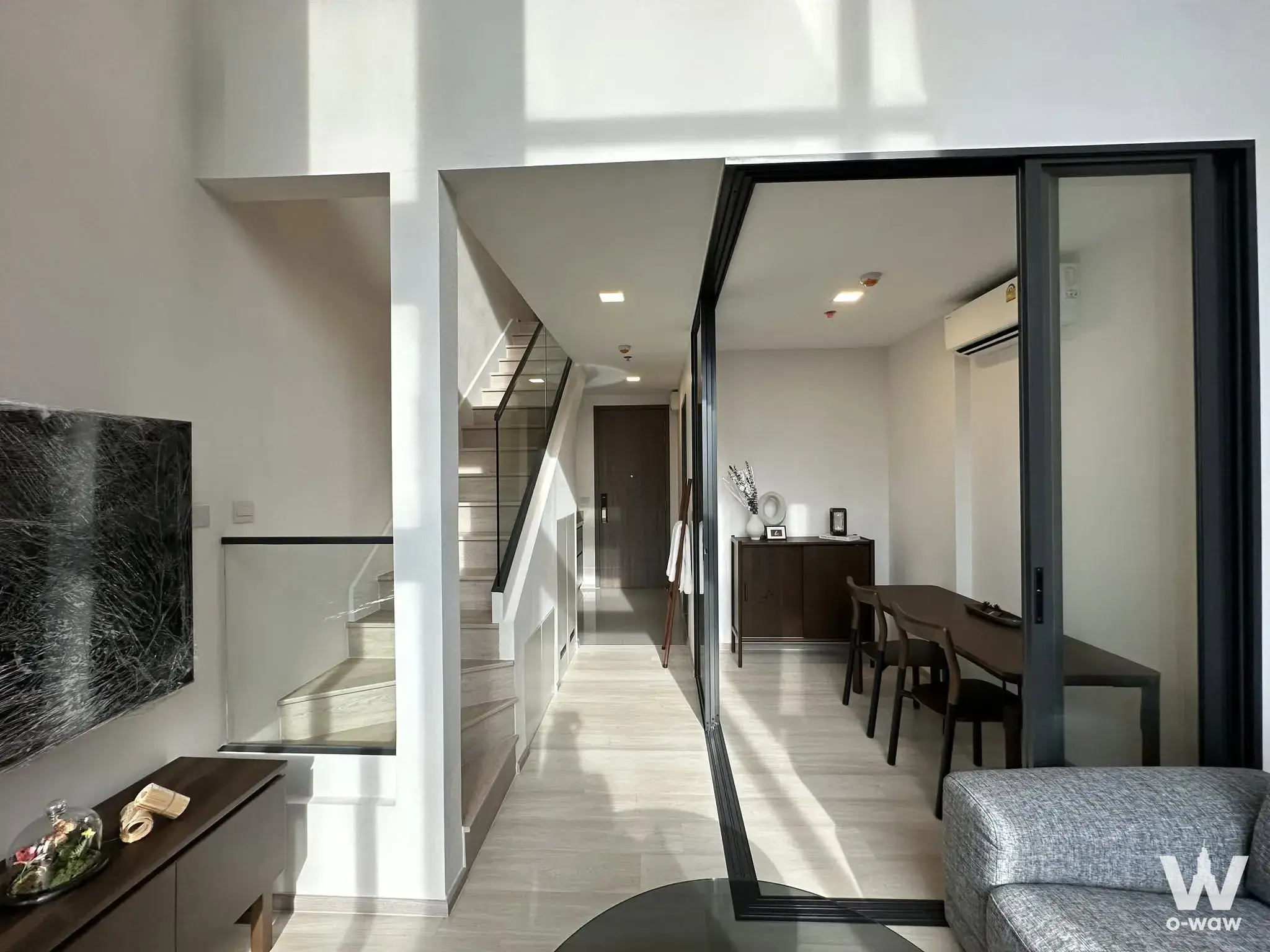 Open-plan living area with dark walnut dining set and glass-railed staircase in this 1-bed condo for sale at The Privacy