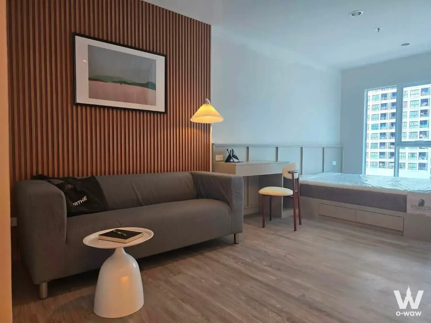 Studio in Regent Home Bangna condo with wooden slat accent wall, grey sofa, and city view
