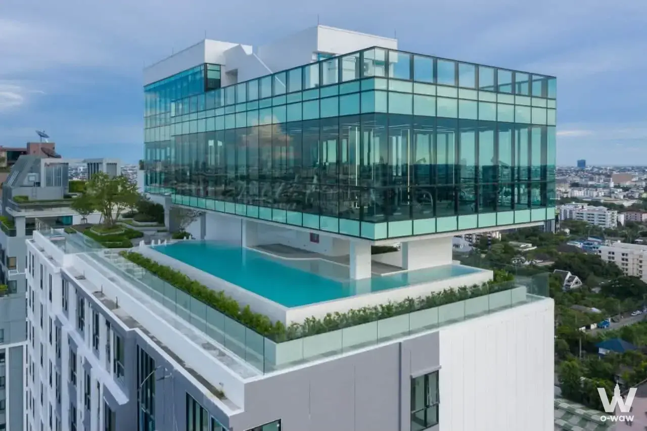 Rooftop infinity pool at Knightsbridge Collage Sukhumvit 107 with gym visible through tinted glass