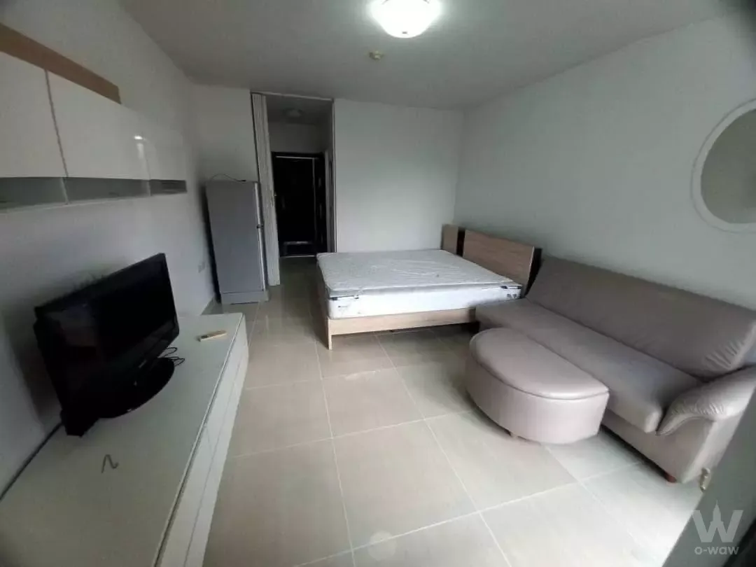 Open-plan studio in a Garden House rental with a queen bed, grey sofa, and circular window