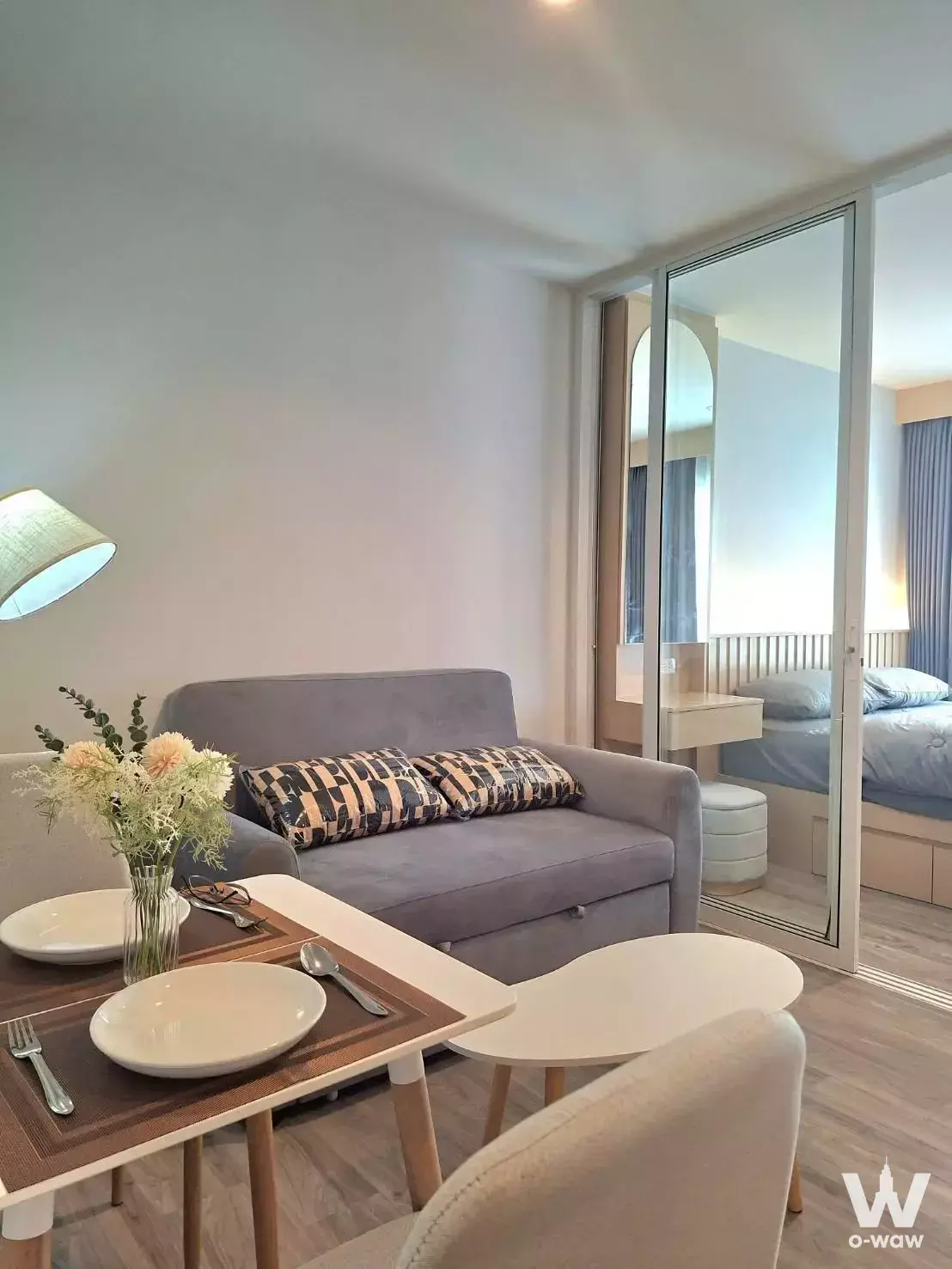 Furnished Regent Home Bangna condo showing a grey sofa, dining table, and bedroom visible through a glass partition