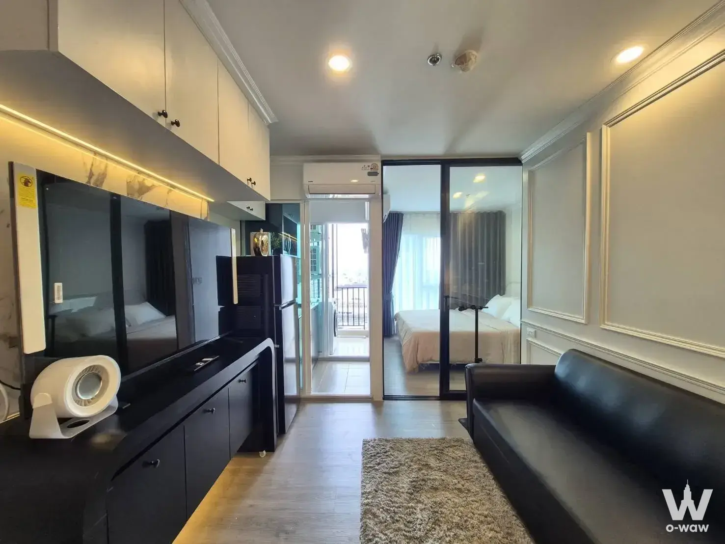 Bright living room in a 1-bed Regent Home Bangna condo featuring a black leather sofa and glass partition to the bedroom