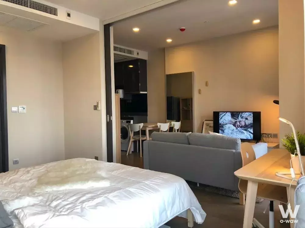 Open-plan studio in Cooper Siam showing queen bed, grey sofa, and kitchen visible through sliding glass partition