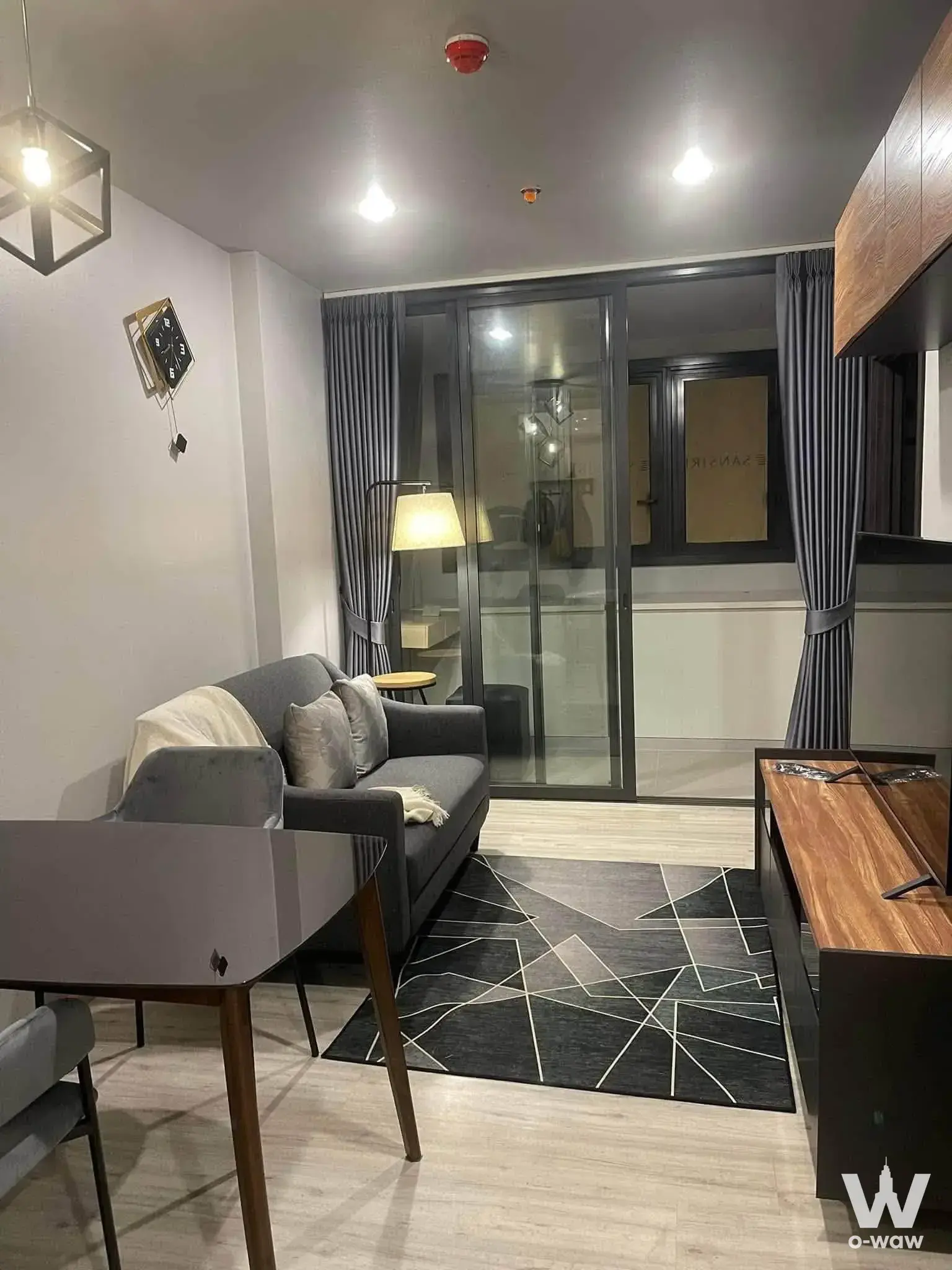 Dark grey sofa and geometric rug in an XT HUAIKHWANG living room with night balcony views
