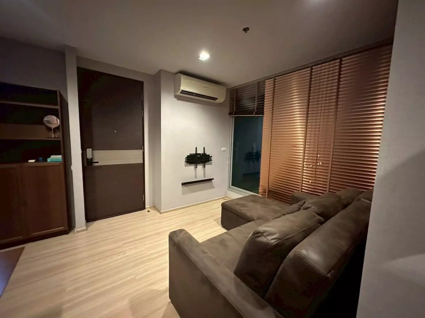 Cozy living room with brown leather sectional and wooden blinds in a 1-bed condo for rent at RHYTHM Sathorn