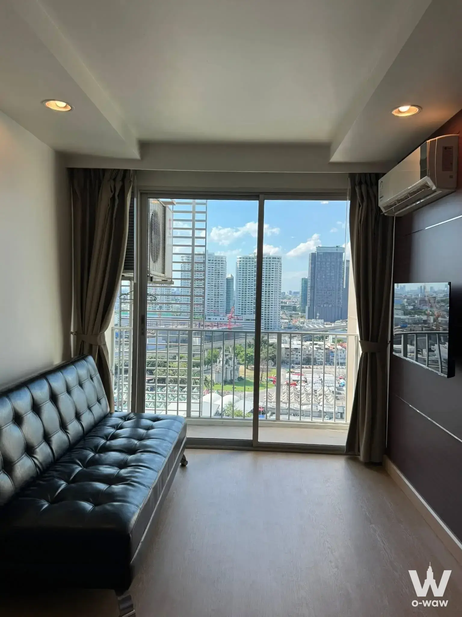 Bright living room in The Park Condominium 1-bed rental featuring black sofa and high-floor city view