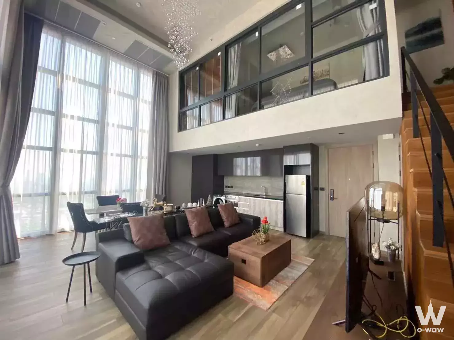 Double-height living room in a 1-bed condo for rent at The Lofts Asoke with leather sectional sofa and mezzanine bedroom