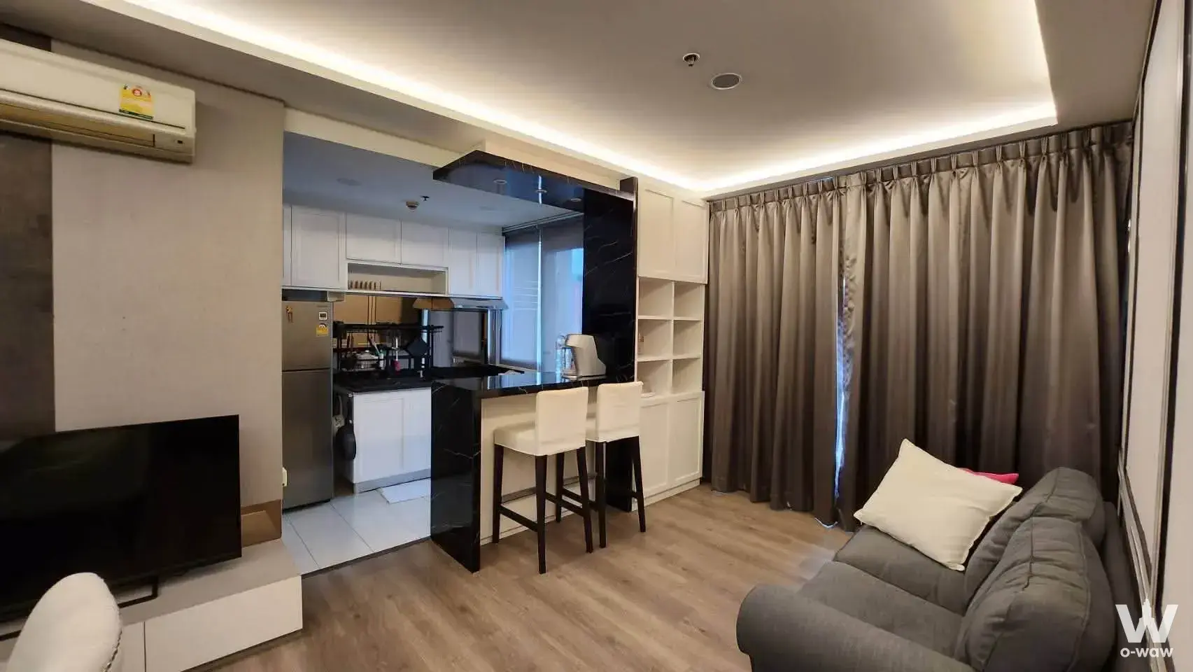 Open-plan living room in Hive Taksin condo with grey sofa and black marble bar counter