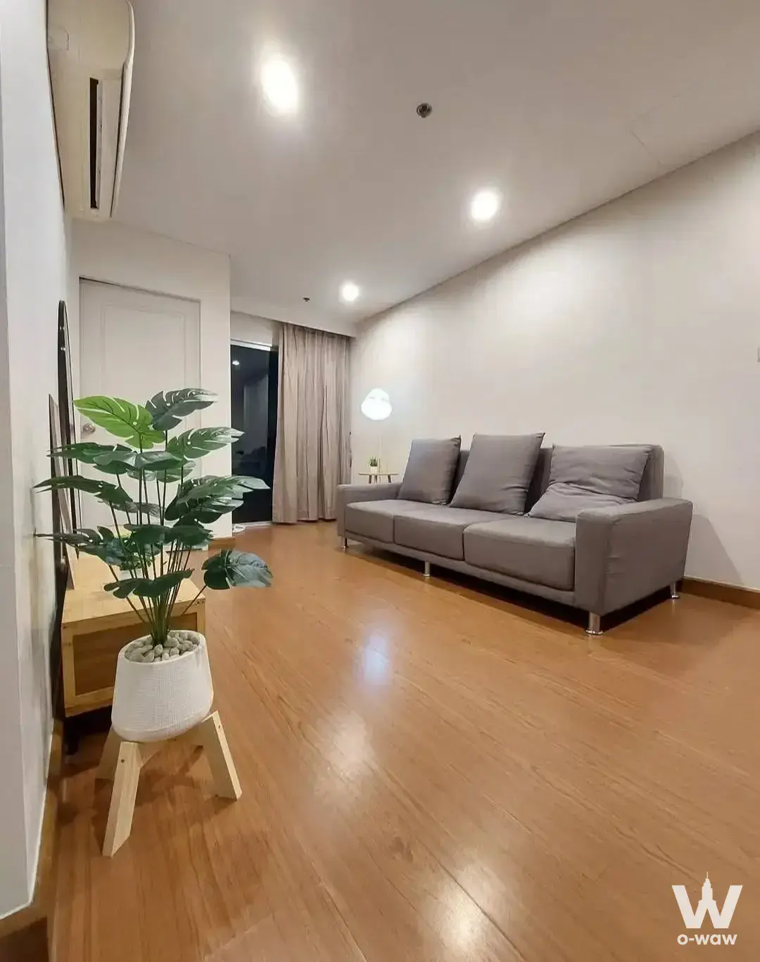 Modern living room with a grey sofa and monstera plant in this Belle Grand Rama 9 condo for rent